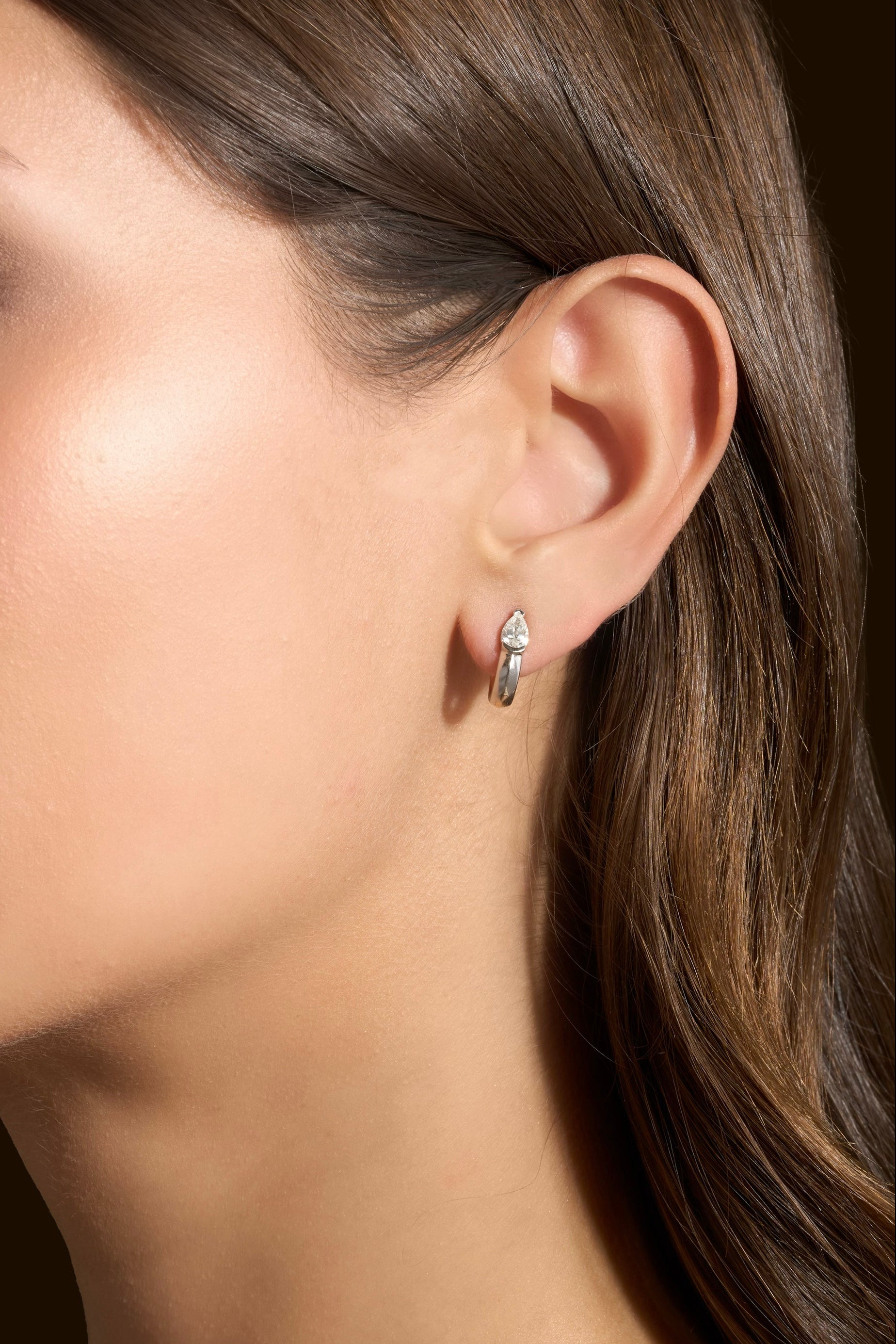 A close-up side profile of a woman wearing a mini hoop featuring pear shaped natural diamonds set in platinum