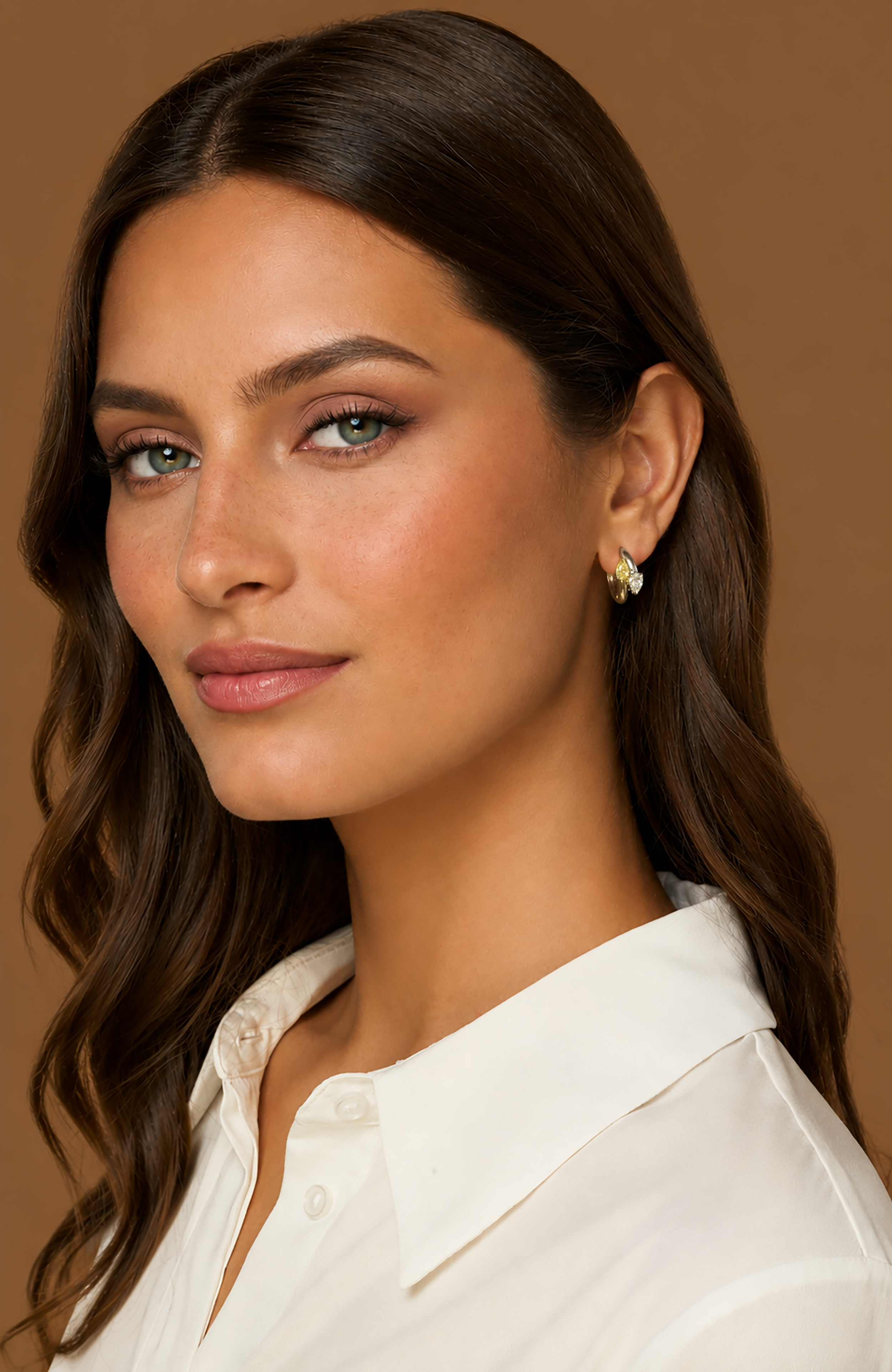 A close-up portrait of a woman wearing 18k yellow gold and platinum hoop earrings with white and yellow pear-shaped natural diamonds in a two tone setting.