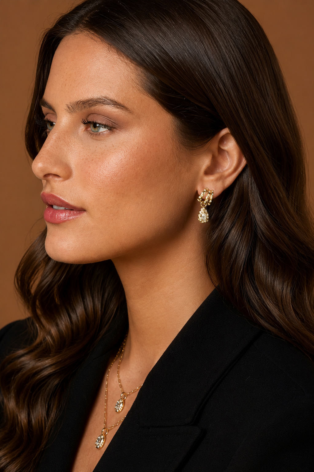 A close-up side profile of a woman wearing 18k yellow gold triple hoop earrings with pear-shaped diamond drop, central pear-shaped natural diamonds and scattered star-set and burnished diamond accents.