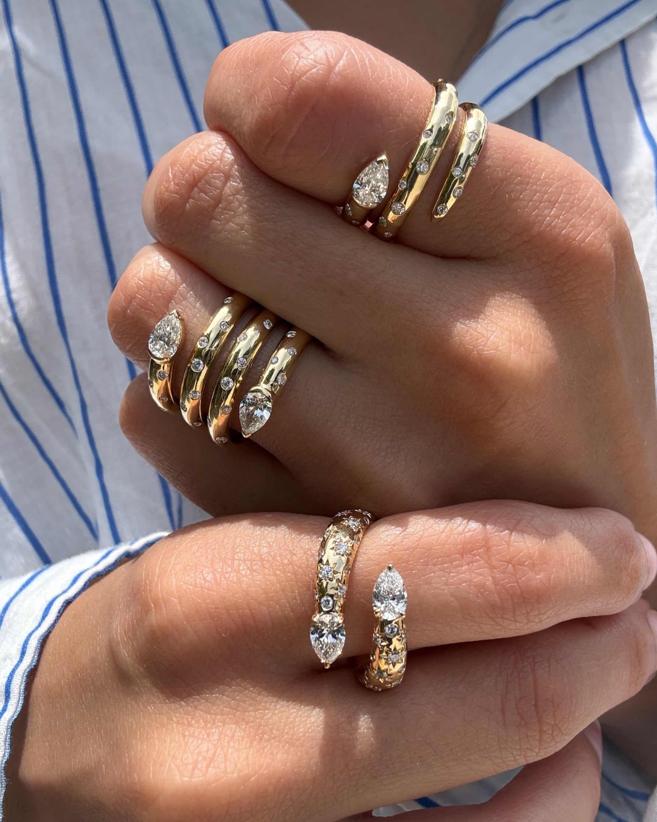 A close-up of a person's hands wearing multiple gold rings featuring 18k yellow with pear-shaped natural diamond and scattered star-set and burnished diamond accents.