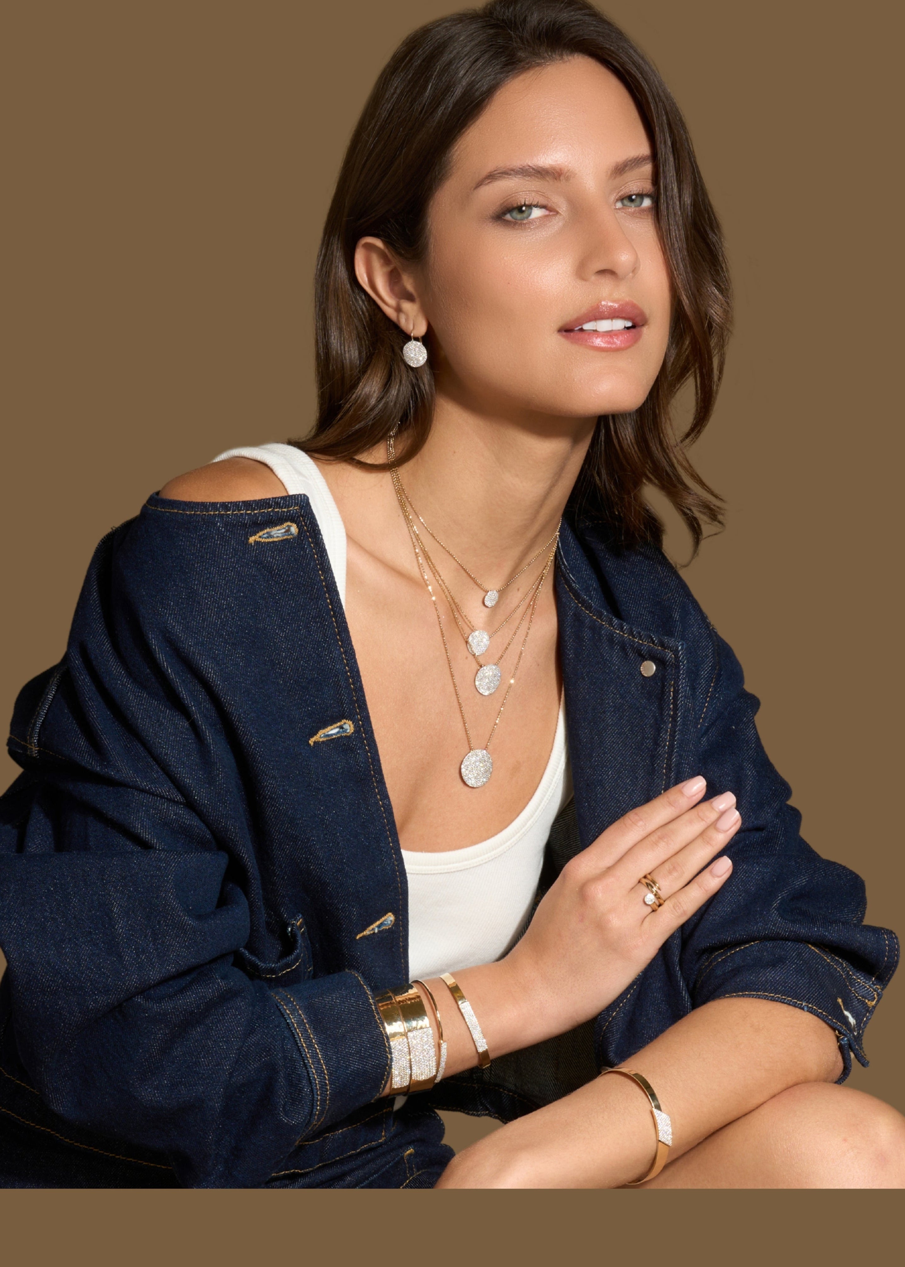 Woman wearing a navy jacket and white top with pave set diamond and 14k gold jewelry on a brown background